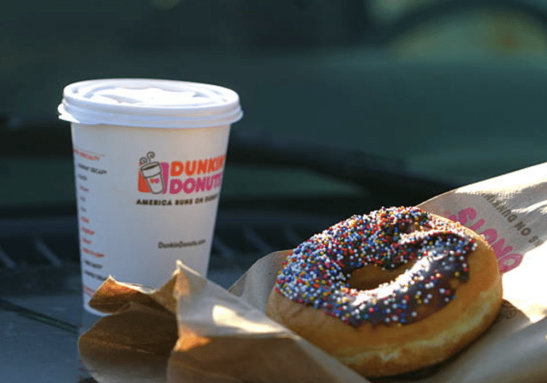 Dunkin' Donuts coffee cup next to a chocolate donut with colorful sprinkles, placed on a paper napkin.